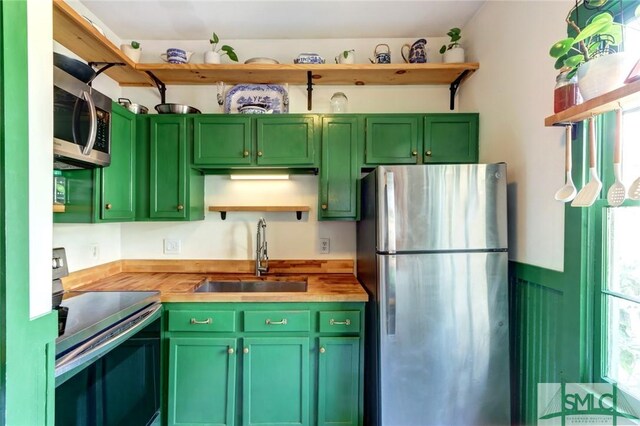 kitchen with open shelves, stainless steel appliances, butcher block counters, a sink, and green cabinetry