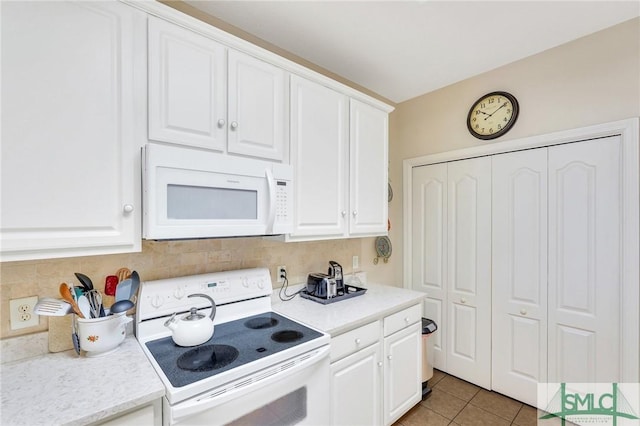 kitchen with light tile patterned floors, white appliances, white cabinetry, light countertops, and decorative backsplash