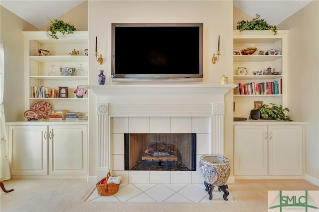 sitting room featuring vaulted ceiling, built in shelves, light carpet, and a tile fireplace