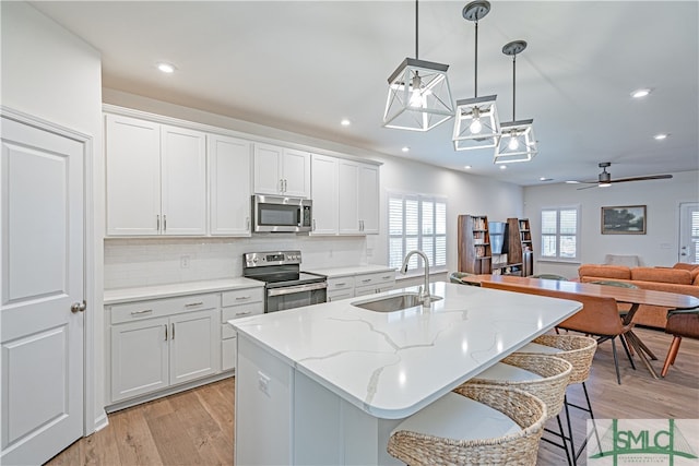 kitchen with light wood-style floors, a kitchen island with sink, stainless steel appliances, and a sink