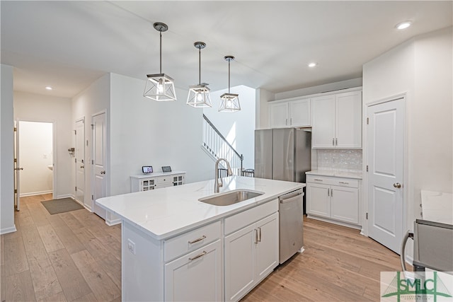 kitchen featuring tasteful backsplash, white cabinets, appliances with stainless steel finishes, light wood-type flooring, and a sink