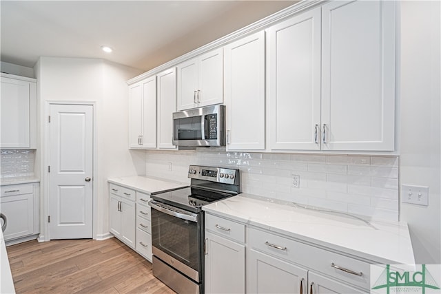 kitchen with stainless steel appliances, light stone counters, light wood-type flooring, and white cabinetry