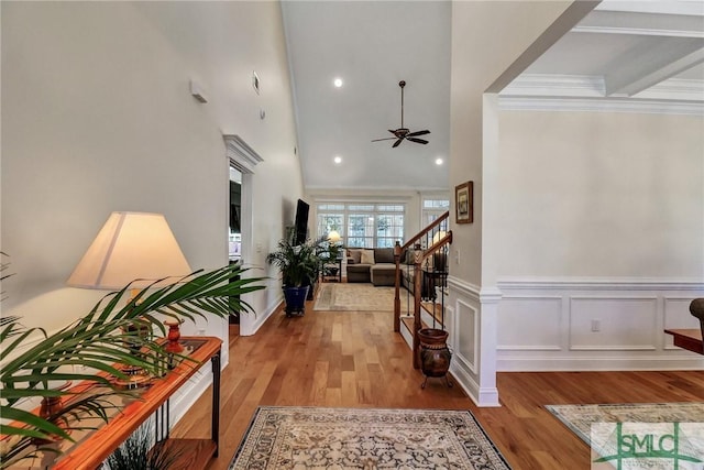 entryway with a ceiling fan, a wainscoted wall, stairway, wood finished floors, and crown molding