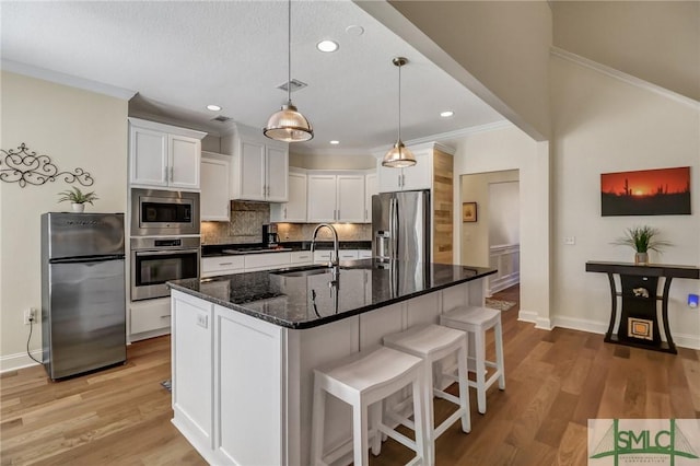 kitchen with white cabinets, a sink, stainless steel appliances, crown molding, and backsplash