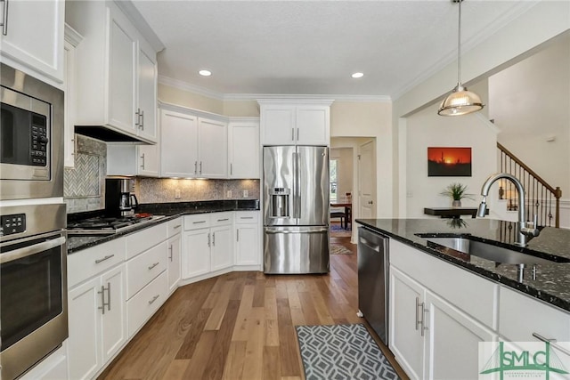 kitchen featuring tasteful backsplash, appliances with stainless steel finishes, white cabinetry, a sink, and wood finished floors