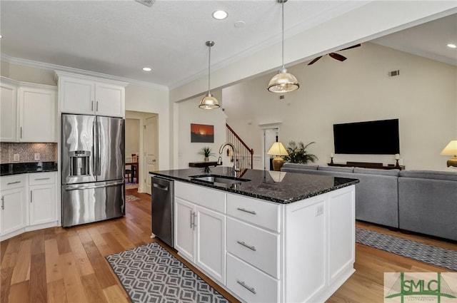 kitchen featuring a sink, appliances with stainless steel finishes, light wood finished floors, dark stone countertops, and tasteful backsplash