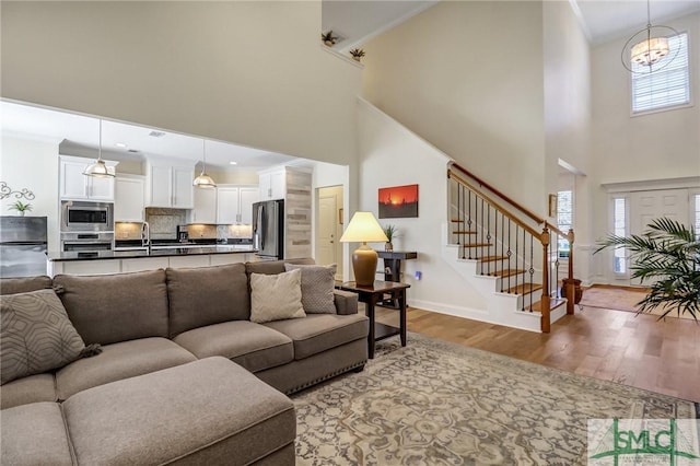 living area featuring wood finished floors, a towering ceiling, baseboards, ornamental molding, and stairway