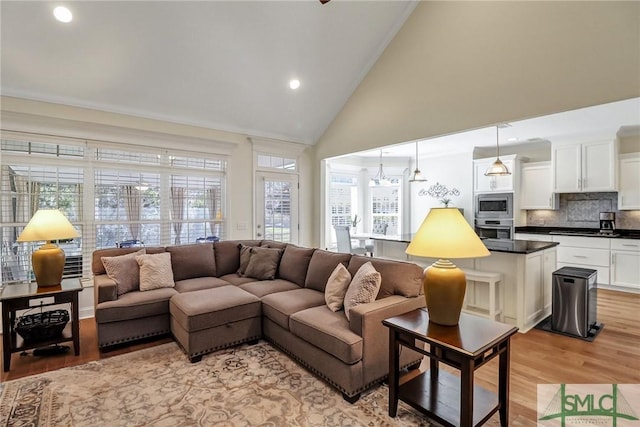 living area with high vaulted ceiling, light wood-type flooring, and recessed lighting