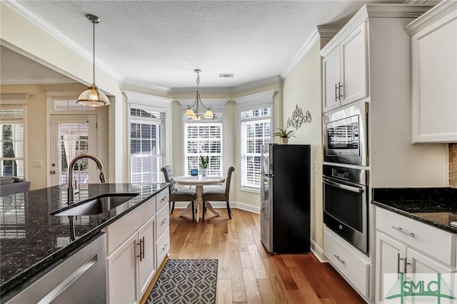 kitchen featuring stainless steel appliances, a sink, visible vents, ornamental molding, and wood-type flooring