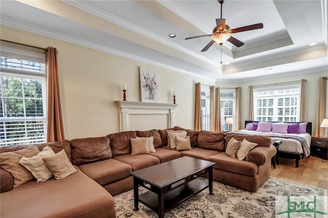 living room with ornamental molding, a tray ceiling, plenty of natural light, and light wood-style flooring