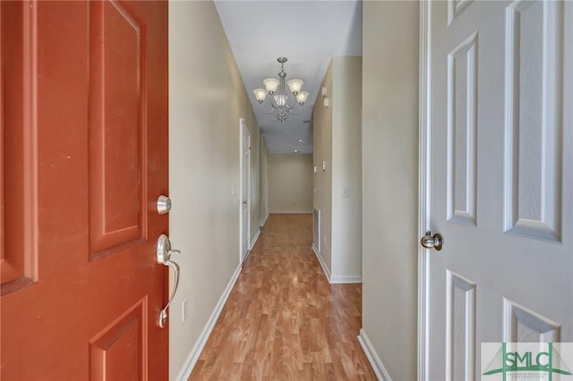 hallway with light wood-type flooring, baseboards, and an inviting chandelier