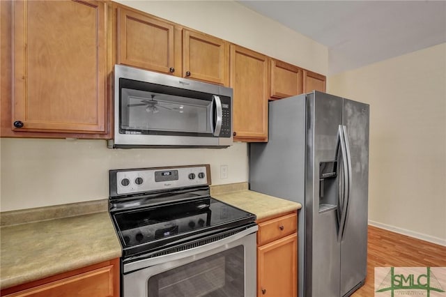 kitchen featuring light wood-type flooring, baseboards, appliances with stainless steel finishes, and light countertops