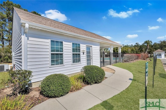 view of side of property featuring a shingled roof, a lawn, central AC unit, and fence