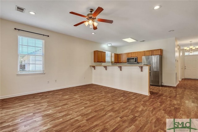 kitchen featuring a breakfast bar area, stainless steel appliances, a peninsula, wood finished floors, and visible vents