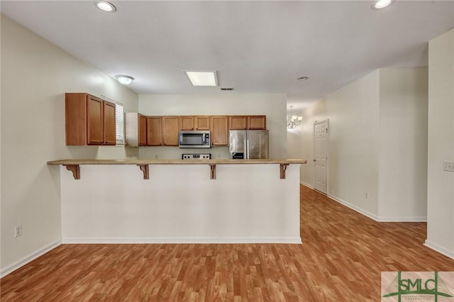 kitchen with a breakfast bar area, a peninsula, appliances with stainless steel finishes, brown cabinets, and light wood finished floors