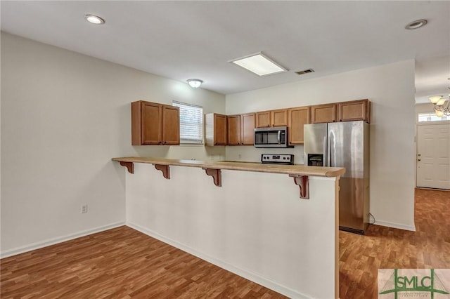 kitchen featuring a peninsula, a breakfast bar, light wood-style floors, appliances with stainless steel finishes, and brown cabinetry