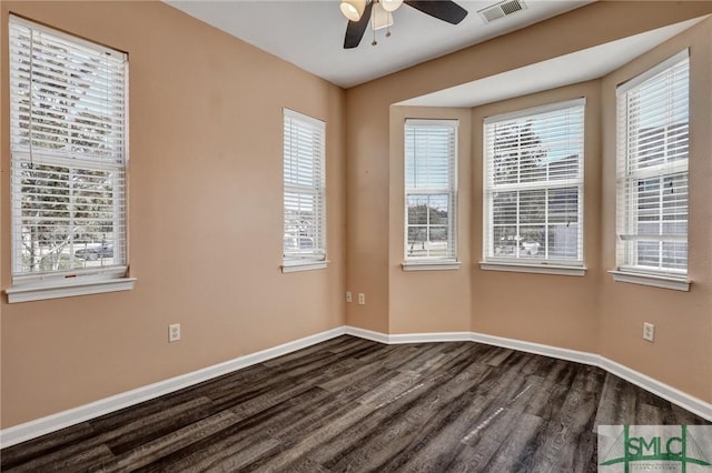 spare room featuring a healthy amount of sunlight, baseboards, visible vents, and dark wood-type flooring