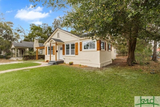 bungalow featuring fence, a front lawn, and stucco siding