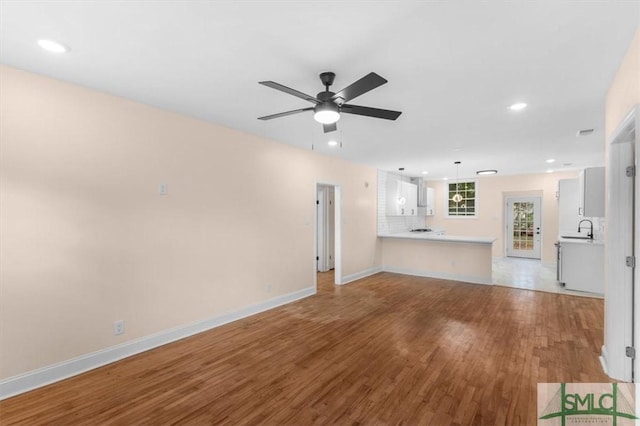 unfurnished living room featuring recessed lighting, ceiling fan, a sink, wood finished floors, and baseboards