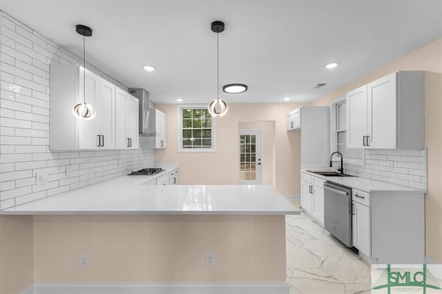 kitchen featuring dishwasher, a peninsula, marble finish floor, wall chimney range hood, and a sink