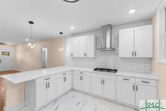 kitchen with marble finish floor, stainless steel gas stovetop, wall chimney range hood, and a peninsula