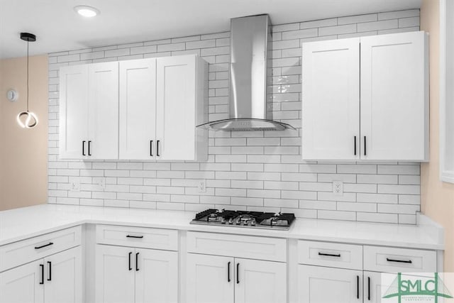 kitchen with stainless steel gas cooktop, white cabinets, light countertops, decorative backsplash, and wall chimney exhaust hood