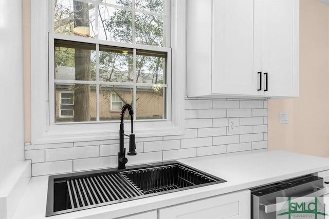 kitchen featuring stainless steel dishwasher, decorative backsplash, a sink, and white cabinets