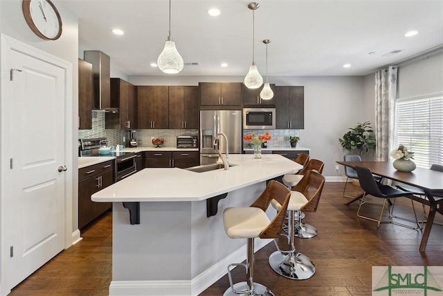 kitchen with a sink, wall chimney range hood, appliances with stainless steel finishes, and a breakfast bar area