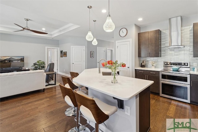 kitchen featuring range with two ovens, a breakfast bar, a sink, light countertops, and wall chimney exhaust hood