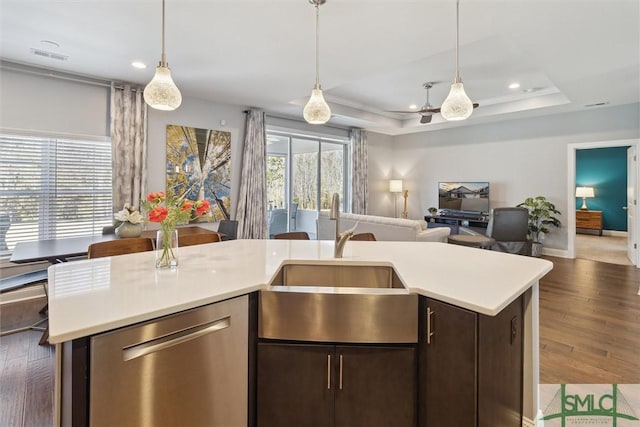 kitchen featuring a raised ceiling, light countertops, stainless steel dishwasher, open floor plan, and a sink