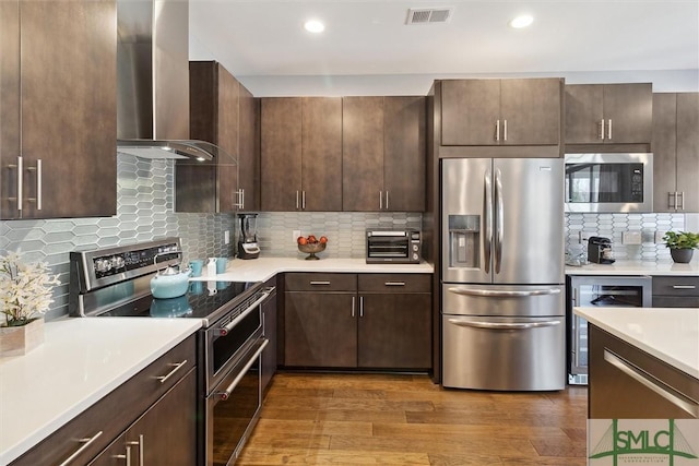 kitchen with visible vents, dark wood-style flooring, stainless steel appliances, light countertops, and wall chimney range hood