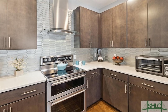 kitchen with wall chimney range hood, range with two ovens, backsplash, and light countertops