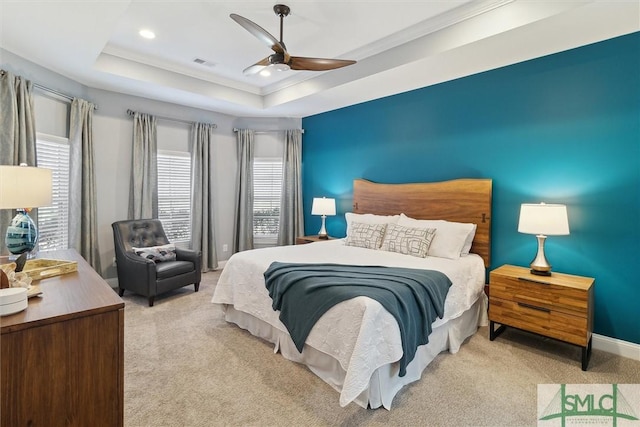 bedroom with ceiling fan, light carpet, visible vents, baseboards, and a tray ceiling