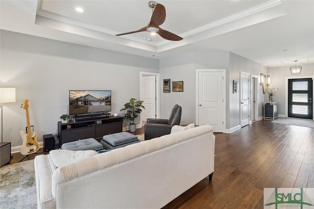 living room with ornamental molding, a raised ceiling, baseboards, and dark wood-style flooring