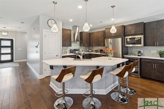 kitchen with wine cooler, stainless steel appliances, light countertops, wall chimney range hood, and a sink