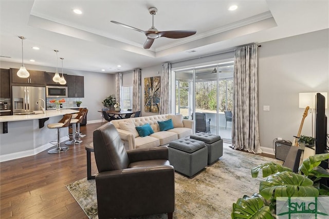 living area featuring dark wood-style flooring, a raised ceiling, a ceiling fan, and baseboards