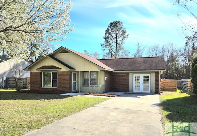 single story home with brick siding, concrete driveway, fence, french doors, and a front yard