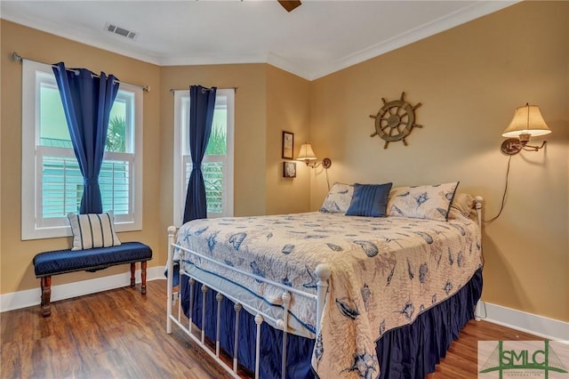 bedroom with ornamental molding, visible vents, baseboards, and wood finished floors