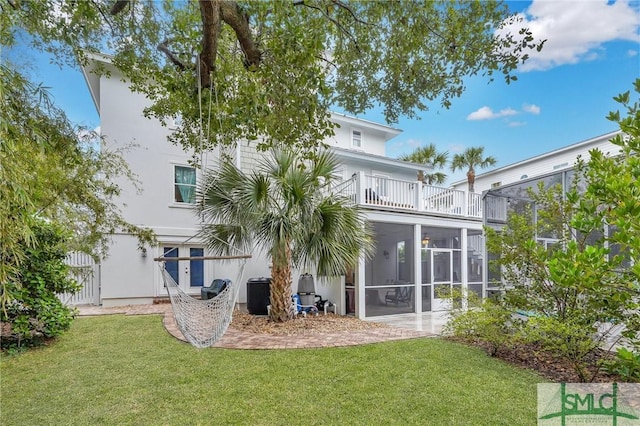 back of house featuring a sunroom, a lawn, a balcony, and stucco siding