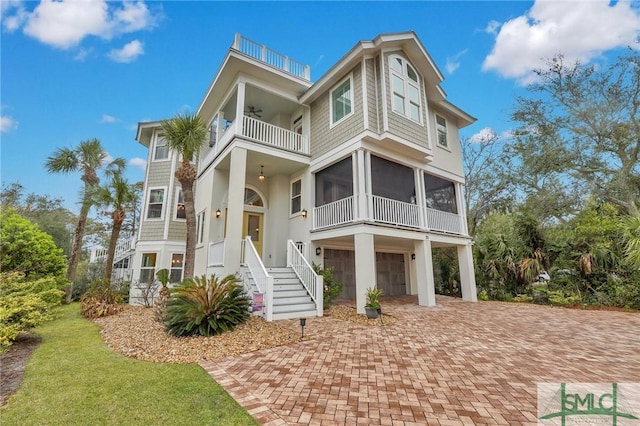 raised beach house with decorative driveway, a sunroom, ceiling fan, a balcony, and a garage