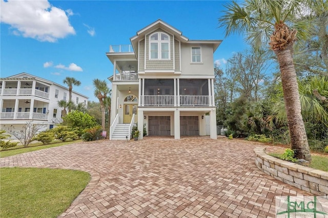 coastal home featuring a sunroom, decorative driveway, a balcony, and a garage