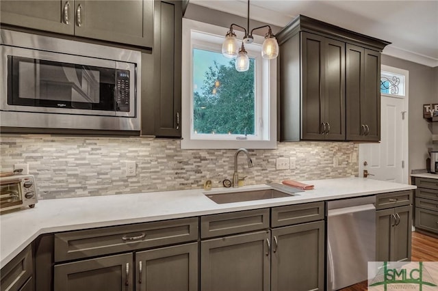 kitchen featuring a sink, light countertops, appliances with stainless steel finishes, tasteful backsplash, and pendant lighting