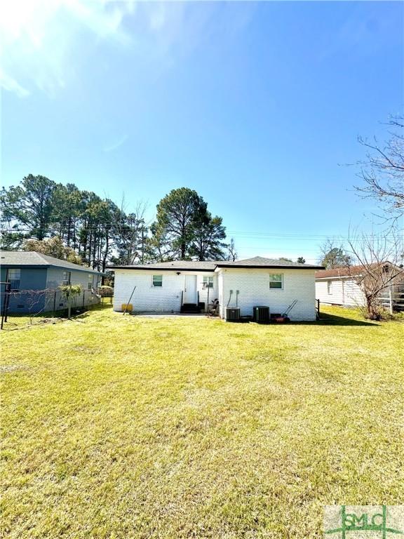 rear view of house with central air condition unit, fence, and a yard