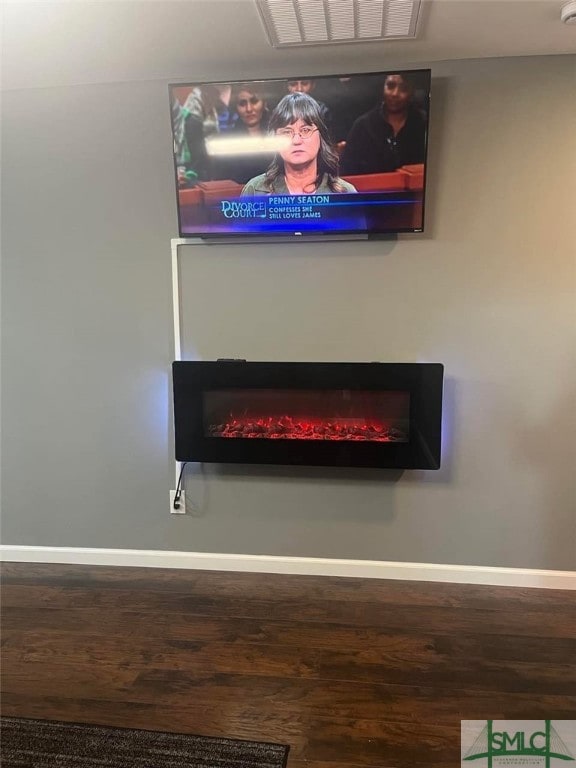 room details with a lit fireplace, wood finished floors, visible vents, and baseboards