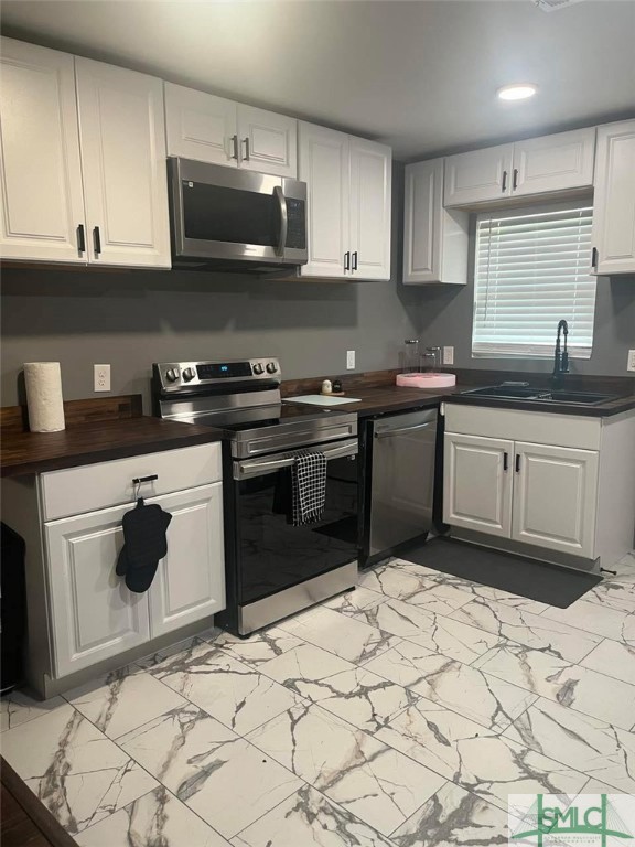 kitchen featuring recessed lighting, stainless steel appliances, a sink, white cabinets, and marble finish floor