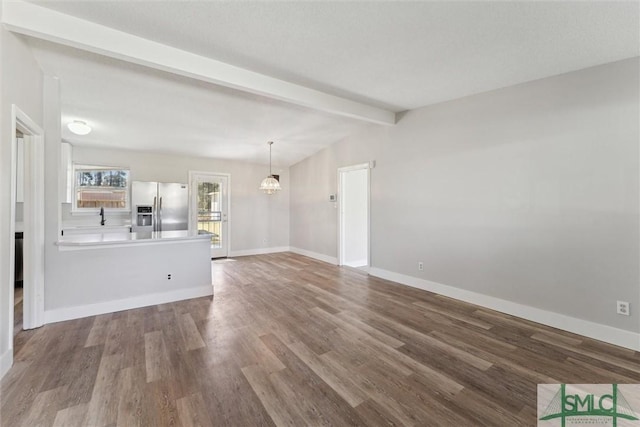 unfurnished living room with vaulted ceiling with beams, a notable chandelier, a sink, wood finished floors, and baseboards