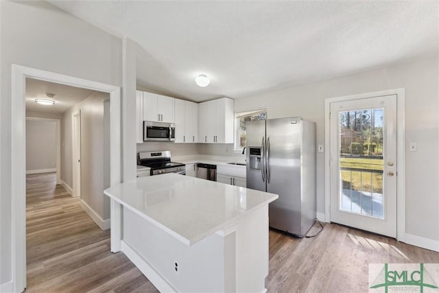 kitchen with light countertops, appliances with stainless steel finishes, light wood-style floors, white cabinetry, and a sink