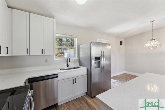 kitchen with decorative light fixtures, light wood-style flooring, appliances with stainless steel finishes, white cabinets, and a sink