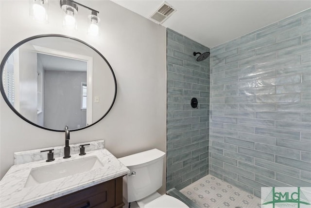 bathroom featuring visible vents, vanity, toilet, and tiled shower