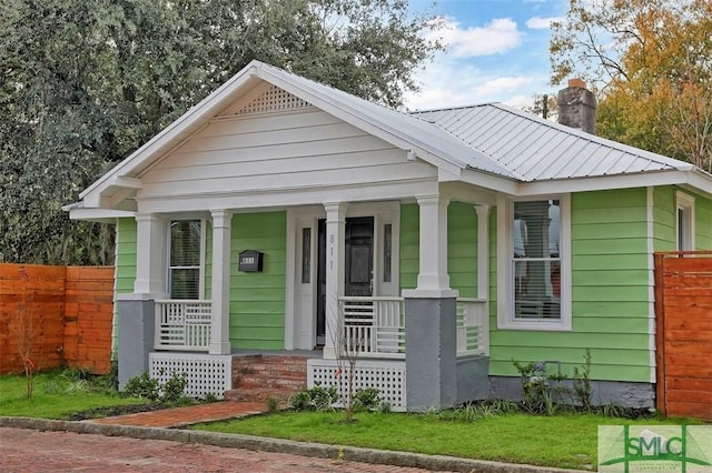 view of front facade with metal roof, covered porch, fence, a chimney, and a front yard